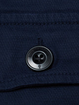 Close-up of the BGpontus Teo Overshirt in Dark Navy by Blue de Gênes, featuring a textured cotton fabric and a black four-hole button engraved with the Blue de Gênes logo along its edge. Horizontal stitching near the button highlights both the relaxed fit and meticulous craftsmanship characteristic of this premium overshirt.