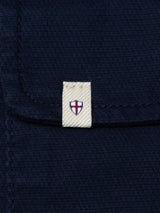 A close-up of the BGpontus Teo Overshirt in Dark Navy by Blue de Gênes shows its textured cotton pocket with a relaxed fit, featuring a small beige tag decorated with a red cross on a white shield, reminiscent of the flag of England.