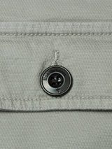 Close-up of the shadow green, honeycomb-textured fabric of the BGpontus Teo Overshirt by Blue de Gênes, featuring a dark button engraved with “Bille de Gens” around its edge and sewn near a stitched seam.