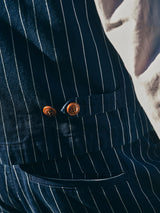 Close-up of the BGkendrick Toll Jacket - Navy Stripe by Blue de Gênes, featuring navy blue stripes and two brown buttons near a pocket, partially illuminated by sunlight.