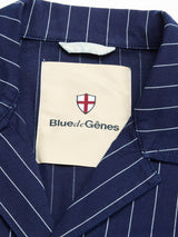 Close-up of the BGkendrick Toll Jacket - Navy Stripe by Blue de Gênes, featuring a navy pinstripe blazer collar and a beige label with a red and white shield, emphasizing the refined details of this striped cotton jacket.