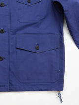 Close-up of the BGcanopy Jacket - Navy Peony by Blue de Gênes, a blue heavy cotton utility jacket with large buttoned pockets, visible buttons, detailed stitching, and a small blue-and-white rope accent near the bottom hem.