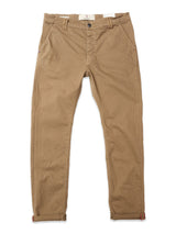 The Blue de Gênes BGpaulo Pavia 1 V2 Chino in Fungi is a tan cotton stretch pant with front pockets, belt loops, and button closure. Laid flat, the hems are slightly turned up to reveal a hint of red lining.