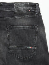 Close-up of the back pocket and waistband of the Vinci G Dark Grey Jeans by Blue de Gênes, made from grey comfort stretch denim, featuring a leather brand patch and a small embroidered detail in red, white, and green on the pocket.