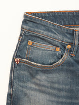 Close-up of Blue de Gênes Vinci Topaz Vintage Jeans - Used in blue denim, highlighting the waistband, front pocket, and a distinctive small shield-shaped patch near the pocket. These regular fit jeans feature orange stitching and brass rivets, and are crafted in Italy from comfort stretch denim.