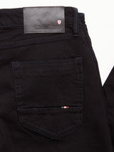 Here’s a revised version of your sentence using the provided product data: Close-up of the back pocket of Vinci Venom Blk Jeans - Dark Denim by Blue de Gênes, featuring a leather label embossed with the brand’s name and a small shield logo above it. The detailed stitching and texture of the comfort stretch twill denim are clearly visible, showcasing Italian craftsmanship.
