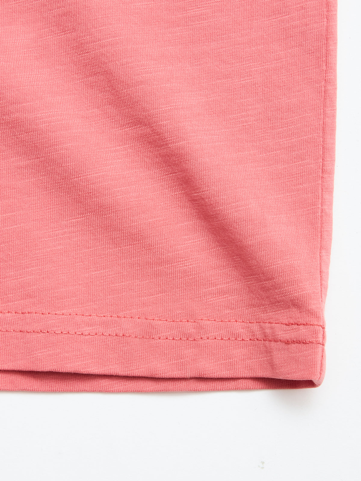 Close-up of the hem on the Blue de Gênes BGoscar T-Shirt in Coral, highlighting the stitching and texture of its regular fit cotton material, laid flat against a white background.