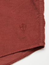 Close-up of the Blue de Gênes Zamboni Velu Shirt in Henna, made from baby corduroy, featuring a small embroidered shield emblem with a cross near the hem. The stitching matches the garment-dyed fabric.