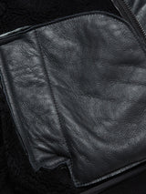 A close-up of black leather fabric with visible texture, stitching, and a zipper on the side, showcasing details from the Rufo Shearling Jacket - Scarab by Blue de Gênes.