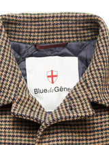 Close-up of the Massone Check Coat collar by Blue de Gênes, featuring a houndstooth-patterned Melton wool and quilted dark lining. A white label inside shows a red shield logo and the brand name.