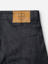 Close-up of the back of BGleroy Jeans - Raw Denim by Blue de Gênes, showcasing a brown leather patch with a shield emblem above the pocket and belt loop. Expertly crafted with innovative denim construction, these five-pocket jeans offer a sleek design for contemporary style.