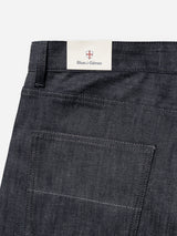 BGleroy Jeans - Raw Denim from Blue de Gênes feature a classic five-pocket design in dark denim, highlighted by a visible back pocket and sturdy belt loops. A white label above the pocket displays the Blue de Gênes name, topped with their distinctive red and white shield logo. Expertly crafted with innovative denim construction, these jeans offer exceptional durability and timeless style.
