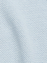 Close-up of the Filo Knit Polo in Blue Water by Blue de Gênes, featuring light blue textured fabric with a waffle-weave pattern and evenly spaced raised squares, highlighted by a gentle fold creating a subtle shadow.
