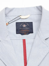 Close-up of a Gabbiano Riga Blazer - Blue Stripe by Blue de Gênes, featuring a light blue and white cotton stripe collar, dark “Blue de Gênes” label with decorative pin on black string, and red fabric lining inside.