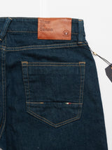 Close-up of the back of Blue de Gênes Vinci Topaz Jeans - Rinse Wash in dark blue, featuring a brown leather brand patch, comfort stretch denim for easy movement, detailed stitching, and a small tricolor tag above the right pocket.