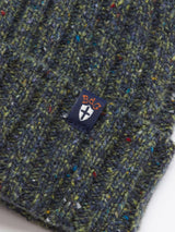 Close-up of the Oscar Melange Beanie in Forest by Blue de Gênes, showing its green knit with blue, red, and yellow flecks and a small navy label featuring an orange BDG logo and a white shield emblem.