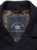 Close-up of the inner label on a Blue de Gênes Peacoat - Dark Navy, featuring a crest and orange stitching. The coat has a dark navy exterior with dark green lining.