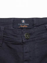 Close-up of the Menzo Dobby Chino - Dark Navy by Blue de Gênes, showing a metal button, belt loops, and a fabric label with the brand name and emblem for a vintage chinos style.