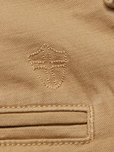 Close-up of the Menzo Dobby Chino in Khaki by Blue de Gênes, showcasing comfort stretch cotton with a stitched shield emblem above a bordered horizontal pocket, emphasizing texture and intricate vintage-style embroidery.