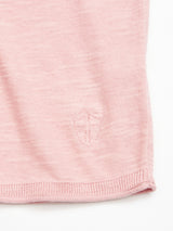 A close-up of the Blue de Gênes Monte Knit in Porcelain Pink shows its soft knit texture, neat edges, and a small embroidered shield emblem near the hem.