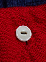 A close-up of a white button sewn onto the navy Tributo Cycling Jersey by Blue de Gênes, with red knitted fabric and blue fabric in the background.
