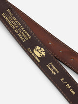 Close-up of the BGualan Belt - Brown by Blue de Gênes, crafted from full-grain leather with gold-embossed text reading "Handmade in Italy" and indicating size L/95 cm. The belt features a decorative crest, classic metal buckle, and distinct Blue de Gênes branding.