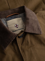 Close-up of the BGjacques AW Coat - Brown by Blue de Gênes, a relaxed car coat made from heavy brown cotton and accented with a corduroy collar. The visible button and interior label—bearing the Blue de Gênes shield logo—add signature touches, while the lining showcases a classic gray herringbone pattern reflecting its workwear inspiration.