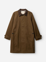 The BGjacques AW Coat - Brown by Blue de Gênes is a brown trench coat with a dark brown corduroy collar, buttoned pockets, and buttoned cuffs, shown on a white background. This coat boasts a classic workwear-inspired design and is crafted from sturdy, heavy cotton fabric.