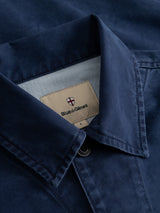 Here’s a rewritten version of your sentence using the provided product data: Close-up of the BGcuddy Nebraska Jacket in blue, showcasing its navy hue, visible button, and an inner beige label bearing the Blue de Gênes brand name with a small shield logo above it, expertly crafted from high-density dobby weave for enhanced texture and durability.