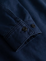 Close-up of the BGcuddy Nebraska Jacket - Blue by Blue de Gênes, highlighting the navy blue sleeve cuff with two black buttons and visible stitching detail, crafted in high-density dobby weave, set against a matching blue fabric background.