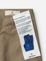 Close-up of the BGliam Nebraska Chino - Brown by Blue de Gênes, featuring a branded label and a fabric patch detailing the Nebraska Chino’s dobby weave fabric characteristics and care instructions, alongside a blue sketch of the trousers.