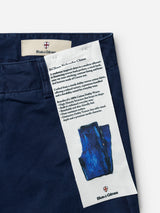 Close-up of navy blue cotton BGliam Nebraska Chino - Blue trousers by Blue de Gênes, featuring a Blue de Gênes label and a fabric patch detailing features such as 100% cotton fabric, high-density dobby weave for added durability, and a blue illustration of pants.