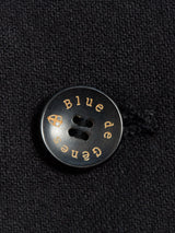 Close-up of a black button on the Canna Carbonio Gillet - Black by Blue de Gênes, engraved in gold with the brand name and a small shield logo.