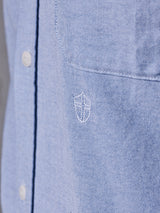 Close-up of the BGsandro Oxford Shirt - Blue by Blue de Gênes, featuring white buttons and a small white embroidered shield logo on the chest pocket area.