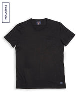 The Sagi Nuovo T-shirt by Blue de Gênes is a regular fit, premium cotton t-shirt in plain black with short sleeves and a small chest pocket. Laid flat on a white background, it features a vertical label on the left reading "THE CLASSICS." This versatile men's wardrobe staple combines style and comfort.