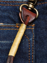 Close-up of a denim pocket with yellow stitching, featuring the Blue de Gênes BGsavino Key Hanger - Brown made from cow leather, wrapped with light-colored thread and attached to a metal clasp.