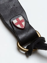 A close-up of the BGsavino Key Hanger - Black by Blue de Gênes, crafted from premium black cow leather, featuring a brass ring and a small shield emblem with a red cross on a white background.