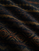 A close-up of the BGrhys Knit - Dark Navy by Blue de Gênes, showcasing a soft, vintage-inspired sweater fabric with a geometric jacquard pattern in rich navy blue, orange, and olive green tones. The detailed woven design features zigzags and diamond shapes, highlighting the textured surface and gentle drape of the material.