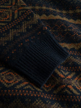 A close-up of the BGrhys Knit - Dark Navy sweater sleeve by Blue de Gênes, showcasing a ribbed dark cuff and a geometric jacquard pattern in dark blue, orange, and olive green tones.
