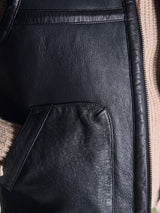 Close-up of the Saga Shearling Gilet - Scarab by Blue de Gênes, highlighting the textured black leather pocket with a glimpse of a beige knitted sleeve on the left. Crafted from premium German Merino sheepskin, this piece ensures exceptional warmth and comfort.