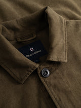 Close-up of the Beech Green BGbarnaba Iro Overshirt by Blue de Gênes, a workwear-inspired collared shirt with a button, featuring the brand’s label and a small shield logo inside the collar.