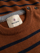Close-up of the BGdaw Stripe Knit - Ginger Bread Orange sweater by Blue de Gênes, featuring a crewneck design with navy stripes, two black buttons near the collar, and a cream label that reads “Blue de Gênes” with a red and white shield logo above the text.