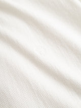 A close-up of the textured white fabric from the BGenrico Tessusto Shirt in Chalk by Blue de Gênes, showcasing its honeycomb-textured cotton and a slightly raised small circular embroidered detail at the center.