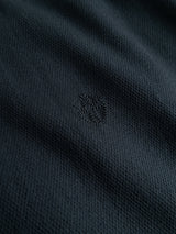Close-up of the textured navy honeycomb fabric of the BGenrico Tessusto Shirt by Blue de Gênes, featuring a small, subtle embroidered logo at the center. The lighting accentuates the intricate pattern and detail of this premium cotton button-down material, ideal for a men’s casual shirt.