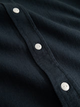 Close-up of the BGenrico Tessusto Shirt in navy by Blue de Gênes, showcasing its dark honeycomb textured fabric with a row of white buttons sewn onto it, highlighting the details of this men’s casual cotton button-down shirt.