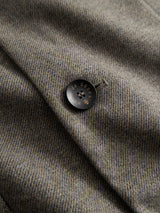 A close-up of the BGFukui Wool Blazer - Grey Mel by Blue de Gênes showcases its refined gray herringbone wool fabric and a distinctive black button adorned with gold letters and symbols. The button is neatly secured through a classic buttonhole—a sophisticated detail that enhances the timeless yet relaxed appeal characteristic of an unstructured blazer.