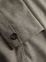Close-up of the Blue de Gênes BGFukui Wool Blazer in Grey Mel, showcasing its grey and beige herringbone-patterned fabric. A black button with subtle engraved text is sewn onto a flap. The fabric forms part of this unstructured blazer, designed for a relaxed fit that balances effortless style and comfort.