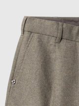 Close-up of the waistband and upper section of the BGkyoto Wool Pant - Grey Mel by Blue de Gênes, featuring belt loops, a button, and a small round pin with a white and red shield design on the pocket. These relaxed tailored trousers in grey melange offer a straight-leg silhouette for versatile styling.