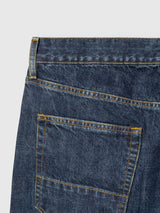 Close-up of the back pocket and waistband of BGmarco Cast Jeans - Denim wash by Blue de Gênes, featuring blue cotton denim with yellow stitching, part of the belt loop, and upper seam, set against a plain white background.