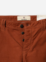 Close-up of BGpaulo Ottawa V3 Trousers in Ginger Bread Orange by Blue de Gênes, crafted from rust-colored dobby corduroy in a slim fit. Features include three exposed black buttons, belt loops, and a visible Blue de Gênes label inside the waistband. A partially visible clothing tag is tucked into the top right.